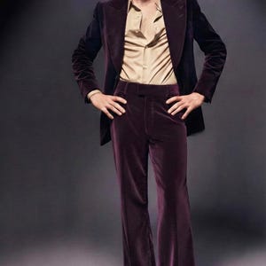 May include: A three-piece suit in a deep burgundy velvet. The suit includes a blazer, matching flared trousers, and a light tan button-down shirt. The brand name "VEMIRA" is visible in the upper left corner.