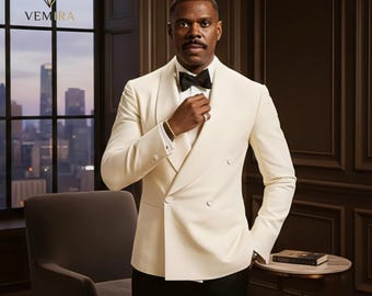 Puede incluir: Un blazer crema de doble botonadura con pajarita negra. El blazer tiene un diseño clásico de solapa y botones. La imagen también muestra pantalones negros y una pulsera dorada. El fondo incluye un horizonte urbano y un logotipo que dice "Vemira".