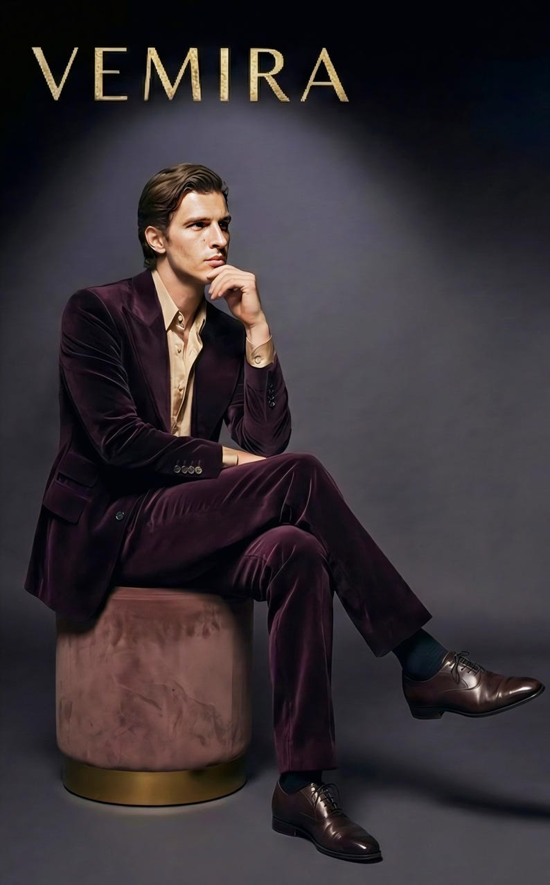May include: A man in a plum velvet suit and a gold-colored shirt sits on a pink ottoman with a gold base. The word "VEMIRA" is displayed above the man. He wears brown leather dress shoes.