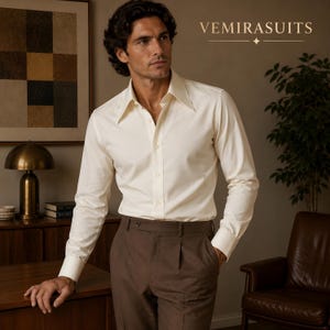 May include: A long-sleeved cream-colored button-down shirt with a pointed collar and brown trousers. The shirt features a front button placket and long sleeves with cuffs. The text VEMIRASUITS is visible in the upper right corner of the image.
