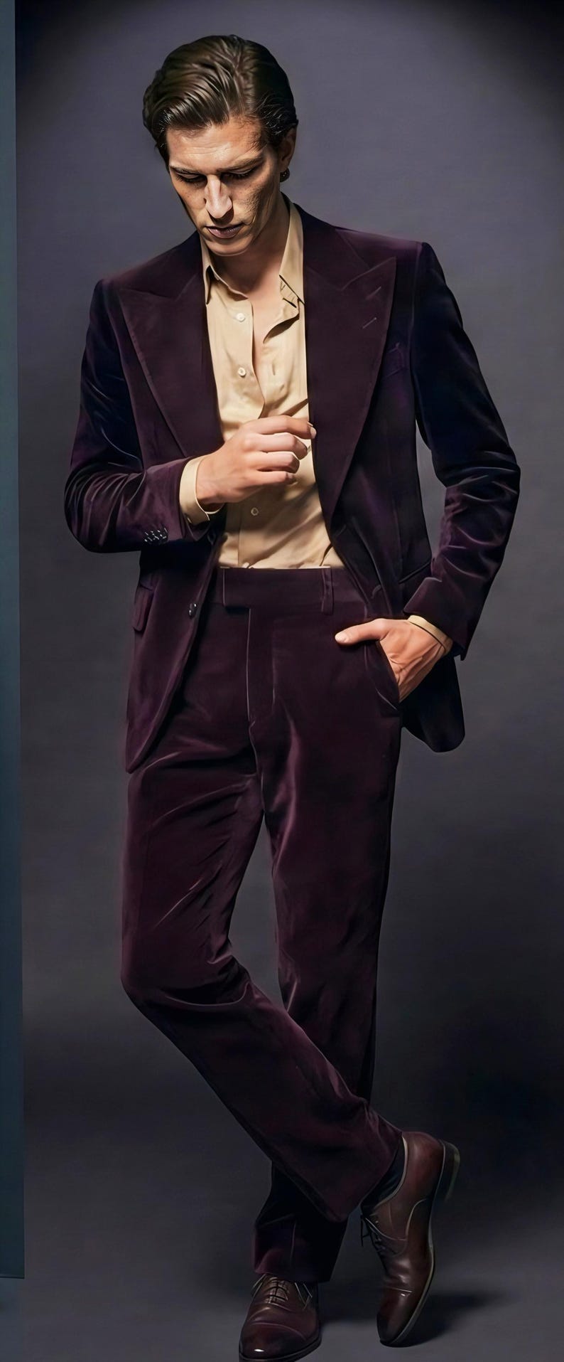 May include: A dark burgundy velvet suit with a matching blazer and trousers. The suit is paired with a light tan button-down shirt. The model is wearing brown leather dress shoes.