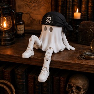 Pode incluir: Uma figura de fantasma branca com membros articulados e sapatos brancos, usando uma bandana pirata preta com um emblema de caveira e ossos cruzados em branco. O fantasma está sentado com uma perna estendida e a outra dobrada.