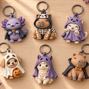 Puede incluir: Seis llaveros con temática de Halloween que muestran varios animales disfrazados: un ajolote vampiro morado, un capibara esqueleto, un gato con capa de fantasma morada, un perro con sábana de fantasma blanca y calabaza, una llama con capa morada y un capibara vampiro.