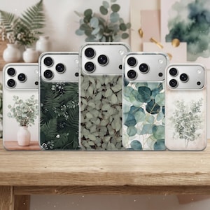 May include: Five clear phone cases with botanical designs. The cases feature various green leaf patterns, including eucalyptus and fern, with a light wood table in the foreground. The cases have a clear border and a camera cutout.