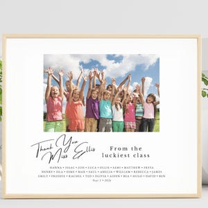 May include: A framed print with a photograph of children with raised arms against a blue sky. The text says "Thank You Miss Ellis From the luckiest class" with a list of names and "Year 1 2026". The frame is a light wood color.