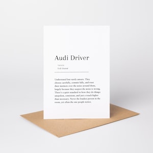 Peut inclure: Une carte de vœux blanche avec le texte imprimé en noir Audi Driver, suivi d'une définition de style dictionnaire et d'une prononciation phonétique. La carte est placée verticalement sur une enveloppe en papier brun clair.