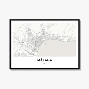 May include: A framed wall art print featuring a detailed grey and white street map of Málaga, Spain. The design displays intricate road networks and coastal geography, with the text MÁLAGA and SPAIN printed in a clean, black sans-serif font below.