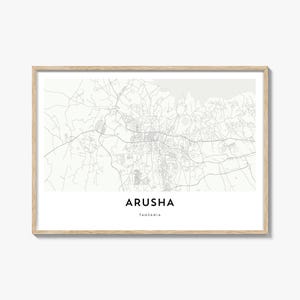 May include: A framed map print of Arusha, Tanzania, in grayscale. The map details the city's layout with roads and buildings. The city name and country are printed in a clean, modern font below the map. The frame is a light wood color.