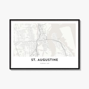 May include: A framed wall art print featuring a light grey and white map of St. Augustine, Florida, USA. The map displays intricate street grids and waterways in a minimalist style, with the text ST. AUGUSTINE FLORIDA, USA printed below.