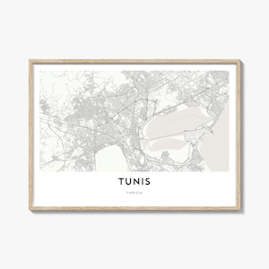 Può includere: Una stampa incorniciata della mappa di Tunisi, Tunisia, in scala di grigi. La mappa dettagliata della città mostra strade e punti di riferimento. La parola "TUNIS" è stampata in grassetto, in nero in basso, con "TUNISIA" sotto. La cornice è in legno chiaro.
