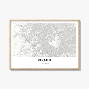 Op de afbeelding: Een ingelijste print met een gedetailleerde kaart van Riyad, Saoedi-Arabië, in grijstinten. De naam van de stad staat onderaan in een modern lettertype. De lijst heeft een lichte houtkleur.