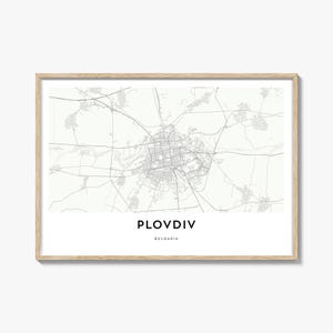 May include: A framed print featuring a detailed grayscale map of Plovdiv, Bulgaria. The city's name is printed in a bold, sans-serif font below the map. The frame is a light wood color, adding a natural touch to the artwork.