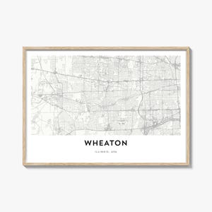 May include: A framed print featuring a detailed map of Wheaton, Illinois, USA. The map is in grayscale, showing streets and buildings. The city name and state are printed in a clean, modern font below the map. The frame is a light wood color.