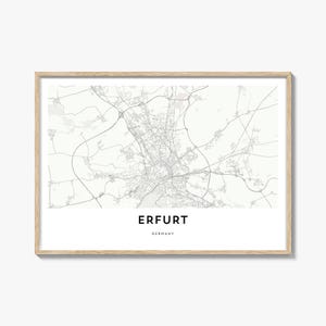 May include: A framed map print of Erfurt, Germany, in grayscale. The city map is detailed, showing streets and infrastructure. The city name "ERFURT" is printed in a bold, black font, with "GERMANY" below it. The frame is a light wood color.