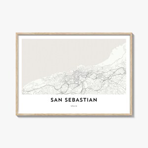 Peut inclure: Impression encadrée d'une carte de Saint-Sébastien, Espagne, dans des tons neutres. La carte détaillée présente un réseau de routes et de caractéristiques géographiques. Le texte "SAN SEBASTIAN" et "SPAIN" est imprimé en bas. Le cadre est de couleur bois clair.