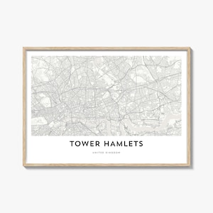 Puede incluir: Una impresión enmarcada del mapa de Tower Hamlets, Reino Unido, en escala de grises. El mapa detalla las carreteras y vías fluviales de la zona. El texto "TOWER HAMLETS" y "UNITED KINGDOM" está impreso en negro en la parte inferior. El marco es de color madera clara.