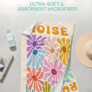 May include: A rectangular microfiber towel featuring a cream-colored background with a repeating pattern of large, stylized flowers in shades of purple, blue, pink, yellow, and orange. The text "OISE" is printed in large, bold, orange letters.