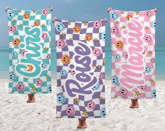 May include: Three beach towels with checkerboard patterns, smiley faces, and star graphics. Each towel has a different color scheme: teal, purple, and pink. The names "Chris", "Roise", and "Marcie" are printed on the towels in a cursive font.