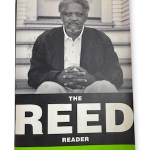 以下が含まれることがあります： イシュマエル・リード著『The Reed Reader』というタイトルの本。表紙には、グレーの髪と髭を生やし、明るいシャツの上に暗いジャケットを着て階段に座っている人物の白黒写真が掲載されています。タイトルは大きな白い文字で書かれています。