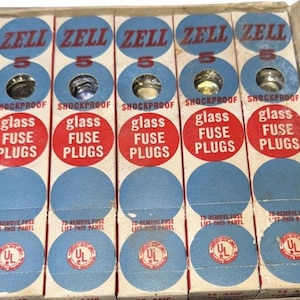 May include: A box of vintage ZELL glass fuse plugs. Each box is labeled with "ZELL", "5", "SHOCKPROOF", and "glass FUSE PLUGS". The boxes are in a cardboard container with blue and red accents and the UL logo.