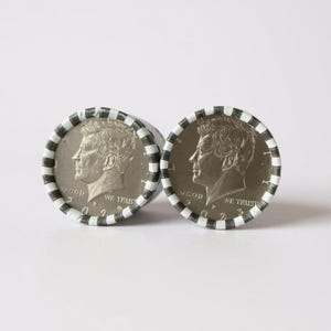 May include: Two rolls of Kennedy half dollars. Each roll is wrapped in a white and black striped paper. The coins show a profile of John F. Kennedy and the words "IN GOD WE TRUST" and "WE TRUST".