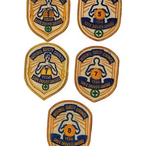 Może przedstawiać: Pięć odznak National Safety Council Safe Driver Award w stylu vintage. Każda naszywka ma kształt tarczy ze złotą obwódką, z postacią, rokiem i napisem "Safe Driver Award". Lata to 1, 5, 7 i 8.