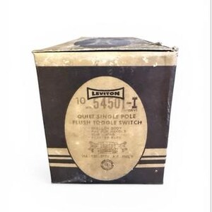 Op de afbeelding: Een vintage doos voor een Leviton Quiet Single Pole Flush Toggle Switch. De doos is donkerbruin met een gouden ovaal label met productinformatie en het Leviton-logo. De doos is licht versleten.