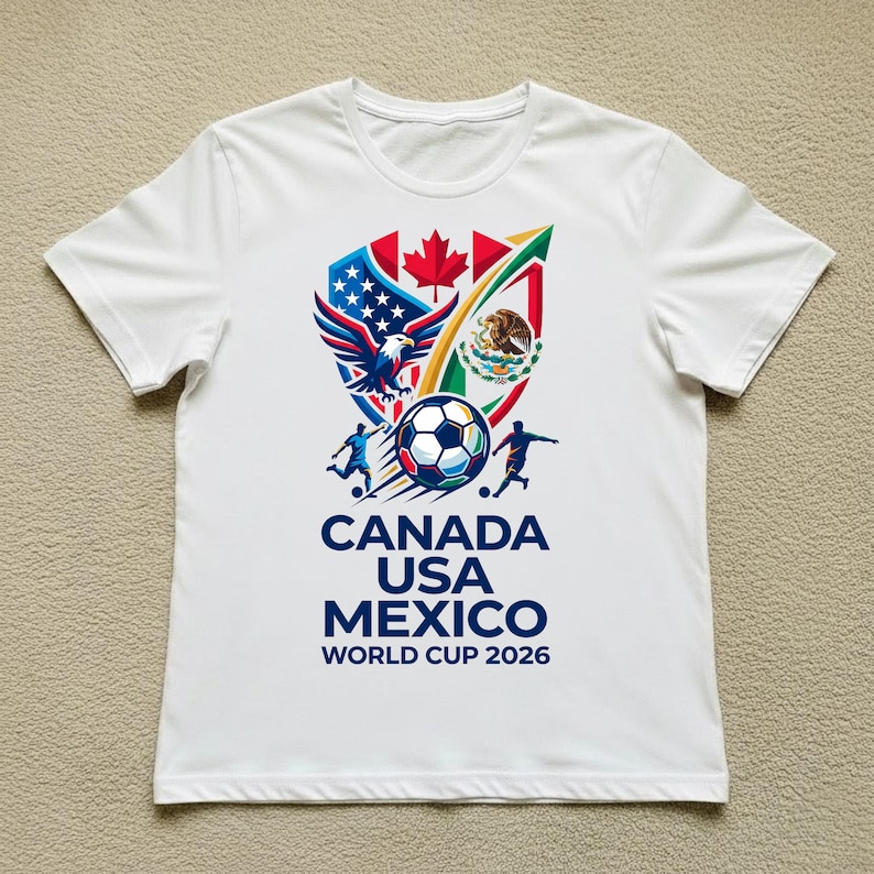 May include: White t-shirt featuring a colorful graphic design for the 2026 World Cup. The design includes the flags of Canada, the United States, and Mexico, along with a soccer ball and the text "CANADA USA MEXICO WORLD CUP 2026".