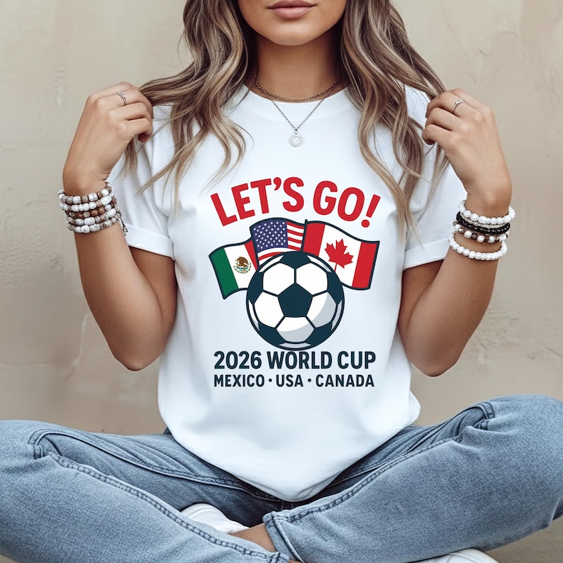 May include: White t-shirt with the text "LET'S GO!" in red. Below the text are flags of Mexico, the USA, and Canada, with a soccer ball in the center. The text "2026 WORLD CUP MEXICO &bull; USA &bull; CANADA" is below the soccer ball.