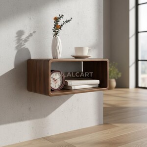 Puede incluir: Estanter&iacute;a rectangular de madera, montada en la pared, con bordes redondeados. Muestra un jarr&oacute;n blanco con flores, una taza y platillo, un reloj y libros. El texto "LALCART" es visible en la estanter&iacute;a.