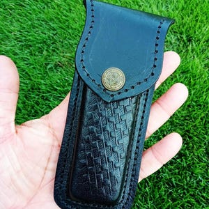 May include: Black leather knife sheath with a basket weave pattern and a brass button. The sheath has a stitched border and the text "X - 640" in the upper left corner.