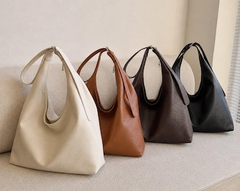 May include: Four hobo bags in a row, each featuring a single shoulder strap and a textured surface. The bags are arranged by color from left to right: cream, tan, dark brown, and black. Each bag has a slouchy, unstructured shape.