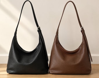 May include: Two hobo bags with a pebbled texture, one in black and one in brown. Each bag features a single shoulder strap with a silver-toned metal buckle adjustment, a curved top opening, and a spacious main compartment with a zipper closure.
