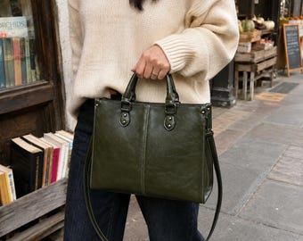 May include: A structured olive green handbag with a smooth finish, featuring dual top handles, silver-toned hardware, and a detachable shoulder strap. The bag has a rectangular silhouette with visible stitching details and a secure top closure.
