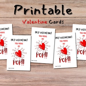 Puede incluir: Tarjetas imprimibles de San Valentín con un diseño de corazón rojo y el texto "Hey Valentine! You Make My POP!!" sobre un fondo de madera. Las tarjetas son blancas con texto rojo y negro.