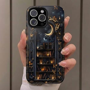 May include: A black phone case featuring a detailed illustration of a bookshelf with books and candles, a crescent moon, and a starry night sky. Gold floral accents frame the design. The case has a glossy finish and a camera cutout.