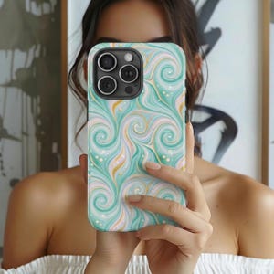 May include: A smartphone case with a swirling pattern in shades of teal, pink, and gold. The case has a glossy finish and a camera cutout with three lenses. The design features a marbled effect with flowing lines and small dot accents.