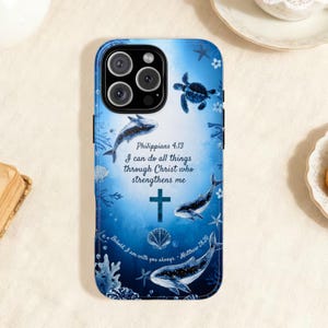 Puede incluir: Funda azul para iPhone con diseño marino, con delfines, una tortuga marina y coral. Incluye el texto "Filipenses 4:13 Todo lo puedo en Cristo que me fortalece" y "Y he aquí yo estoy con vosotros todos los días."