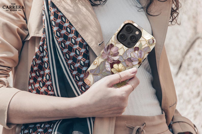 Op de afbeelding: Een smartphonehoesje met een bloemenpatroon in glas-in-loodstijl in paarse, roze en gouden tinten op een cr&egrave;mekleurige achtergrond. Het ontwerp bevat gedetailleerde donkere omlijningen en een uitsparing voor de camera in de linkerbovenhoek.