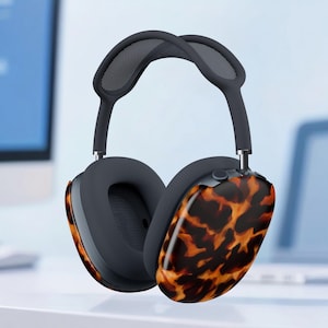 May include: Over-ear headphones with a dark gray headband and earcups. The earcups have a tortoiseshell pattern in shades of brown and orange. The headphones are suspended in the air against a light blue background.