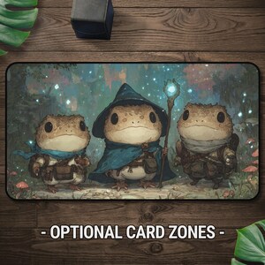 Peut inclure: Un tapis de jeu rectangulaire illustrant trois crapauds anthropomorphes dans une forêt. Le crapaud central porte un chapeau et une cape de magicien bleus et tient un bâton lumineux. Le texte OPTIONAL CARD ZONES est imprimé en bas.