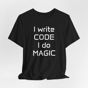 Peut inclure: T-shirt noir avec le texte blanc "I write CODE I do MAGIC". Le t-shirt a un col rond et des manches courtes. Le texte est centré sur le devant du t-shirt.