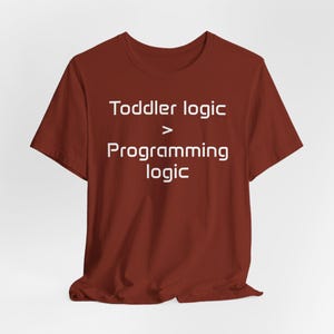 May include: A maroon t-shirt featuring the white text "Toddler logic > Programming logic". The short-sleeved top has a crew neck design. The text is centrally positioned on the front of the garment, which appears to be made of cotton.