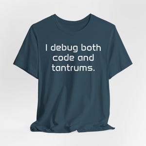 May include: A teal t-shirt featuring the white text: "I debug both code and tantrums." The shirt has a crew neck and short sleeves. The fabric appears soft and comfortable.
