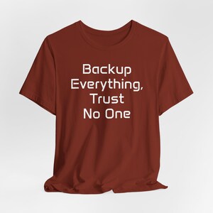 May include: A maroon t-shirt with the white text "Backup Everything, Trust No One". The short-sleeved shirt is made of a soft material and is displayed on a white background. The text is centered on the front of the shirt.