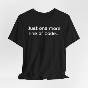 Peut inclure: T-shirt noir avec le texte blanc "Just one more line of code...". Le t-shirt a un col rond et des manches courtes. Le tissu semble doux et confortable.