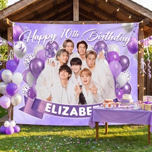 May include: A purple birthday backdrop featuring the text Happy 10th Birthday and ELIZABETH, decorated with illustrations of balloons and a group of seven people in white clothing. The banner is displayed outdoors behind a table with a cake.