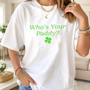 May include: White t-shirt with the text "Who's Your Paddy?" in green, along with a green four-leaf clover graphic. The shirt is a casual, oversized fit.