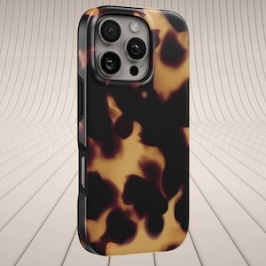 Puede incluir: Una funda protectora para teléfono con un diseño de carey en tonos marrones y amarillos. La funda tiene un borde negro y cubre las lentes de la cámara del teléfono.