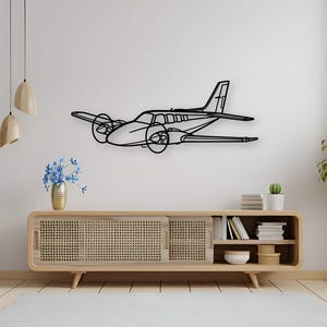 May include: Black metal airplane wall art. The decorative piece features a detailed outline of a twin-engine aircraft, including propellers, wings, and tail. It is mounted on a white wall above a wooden cabinet.